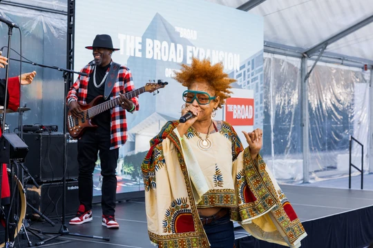 Woman singing in the forefront of a stage with a man playing bass on the stage behind her