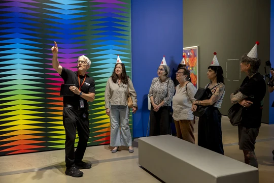 A museum tour guide in the Jeffrey Gibson exhibition talking to a group of visitors