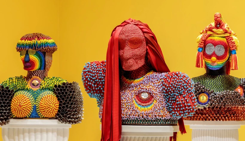 Three beaded multi-color busts with fringed and fabric hair against a yellow background