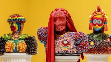 Three beaded multi-color busts with fringed and fabric hair against a yellow background