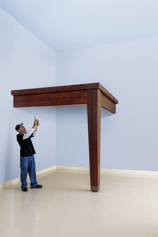A young man in a black shitr and denim jeans and hat standing underneath Robert Therrien's oversized sculpture of a table leg