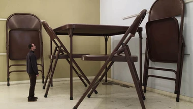 Oversized brown folding chair with a man next to it for size comparison